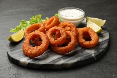 Photo of Fried squid rings, lime, lettuce and sauce on black table, closeup