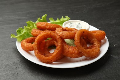 Photo of Fried squid rings served with sauce on black table, closeup