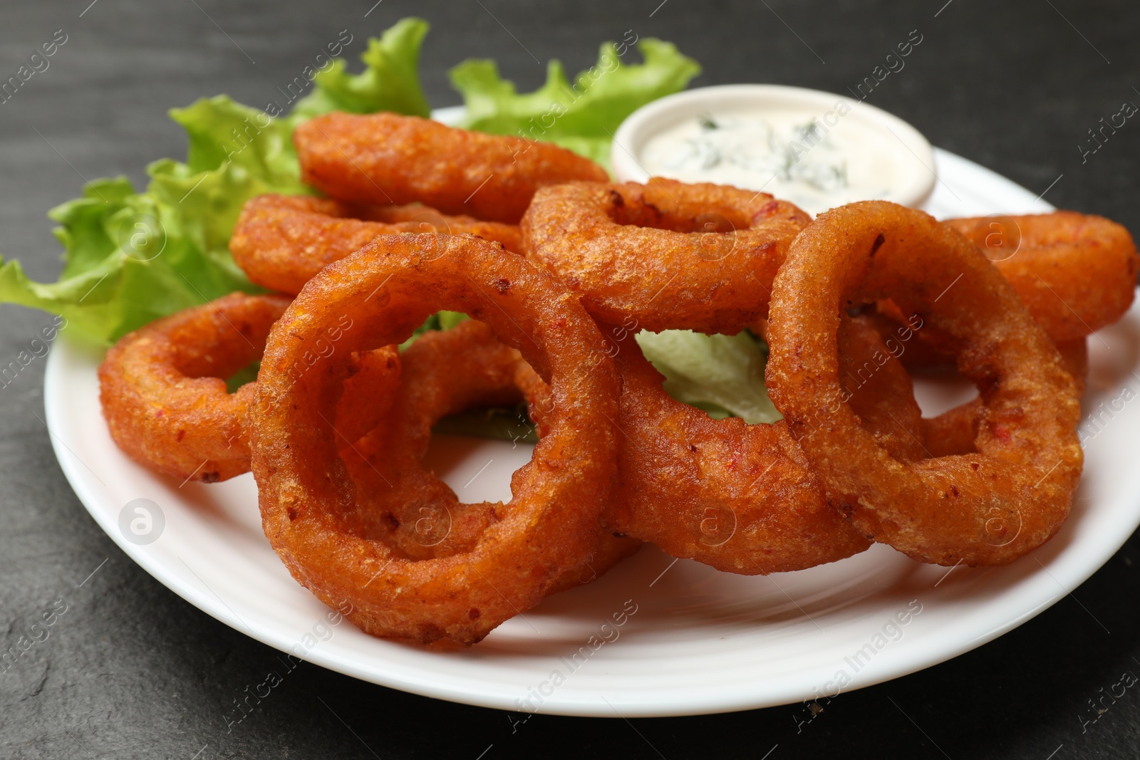 Photo of Fried squid rings served with sauce on black table, closeup