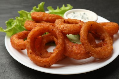 Photo of Fried squid rings served with sauce on black table, closeup