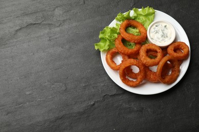 Photo of Fried squid rings served with sauce on black table, top view. Space for text