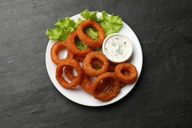 Photo of Fried squid rings served with sauce on black table, top view