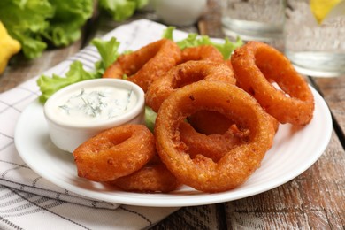 Photo of Fried squid rings served with sauce on wooden table, closeup