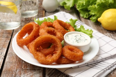 Photo of Fried squid rings served with sauce on wooden table, closeup