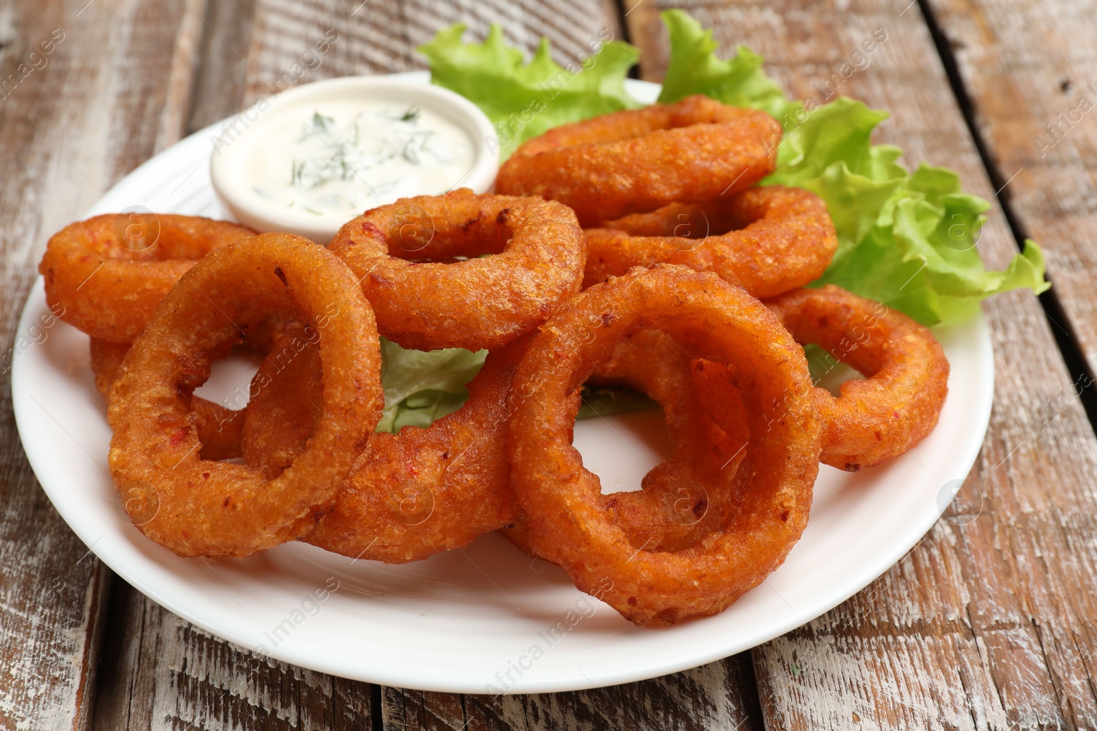 Fried squid rings served with sauce on wooden table, closeup Photo of Fried squid rings served with sauce on wooden table, closeup