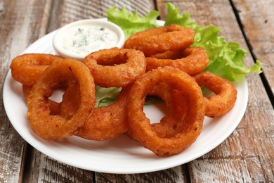 Photo of Fried squid rings served with sauce on wooden table, closeup