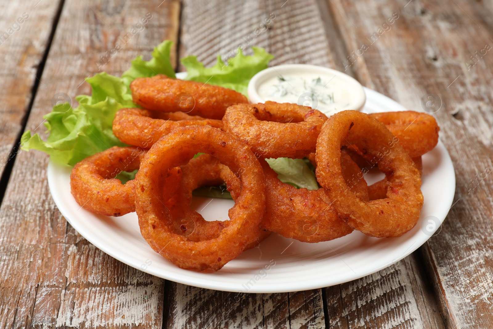 Fried squid rings served with sauce on wooden table, closeup Photo of Fried squid rings served with sauce on wooden table, closeup