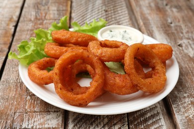 Photo of Fried squid rings served with sauce on wooden table, closeup