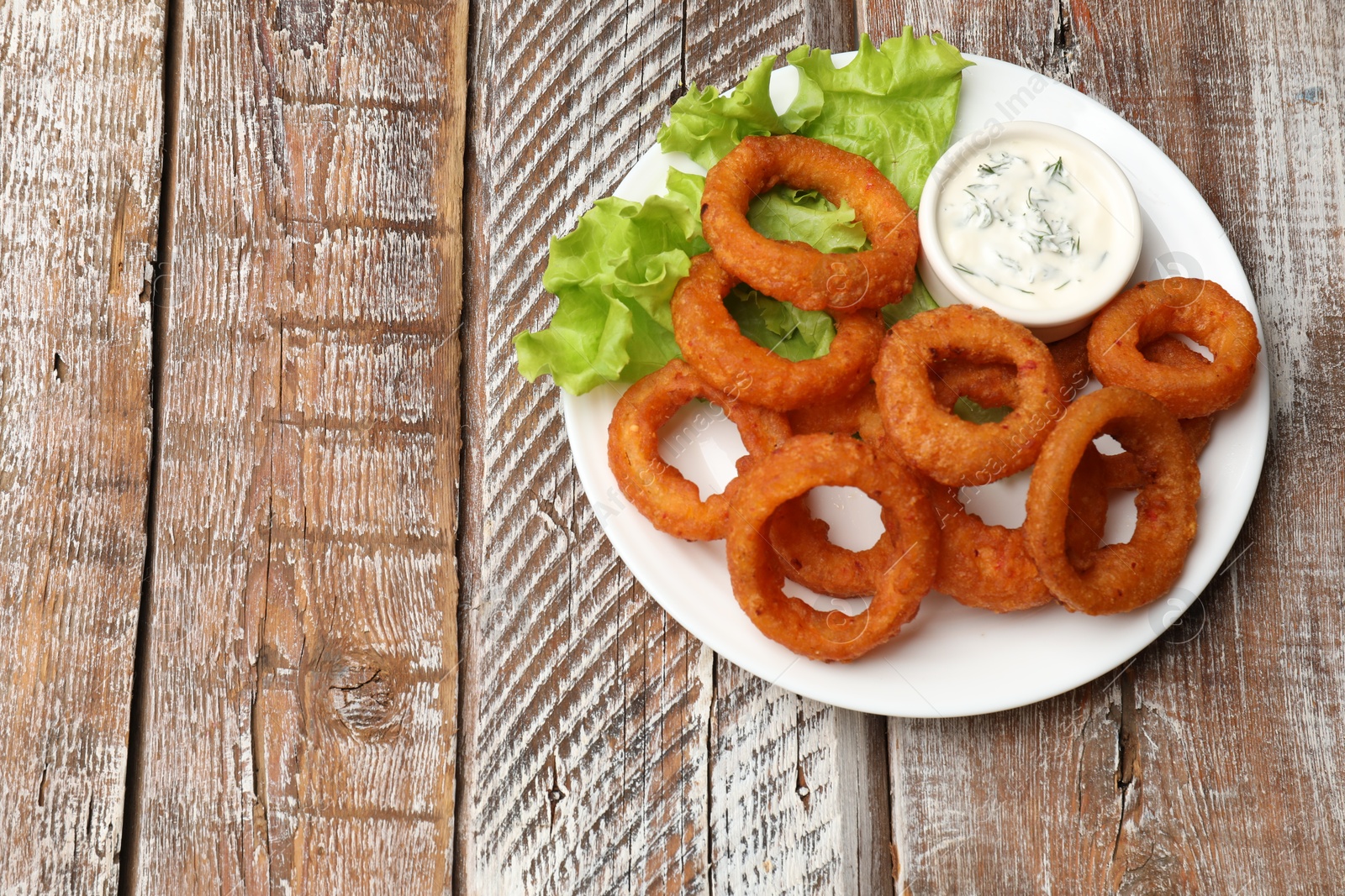 Fried squid rings served with sauce on wooden table, top view. Space for text Photo of Fried squid rings served with sauce on wooden table, top view. Space for text