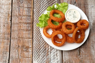 Photo of Fried squid rings served with sauce on wooden table, top view. Space for text