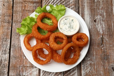 Photo of Fried squid rings served with sauce on wooden table, top view