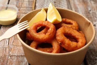 Photo of Fried squid rings, lemon and sauce on wooden table, closeup