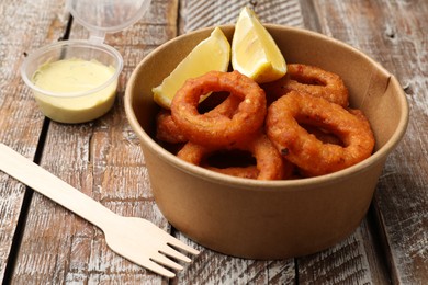 Photo of Fried squid rings, lemon and sauce on wooden table, closeup
