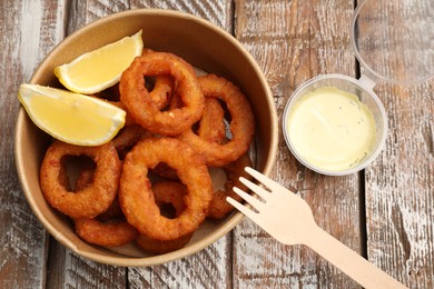 Photo of Fried squid rings, lemon and sauce on wooden table, flat lay