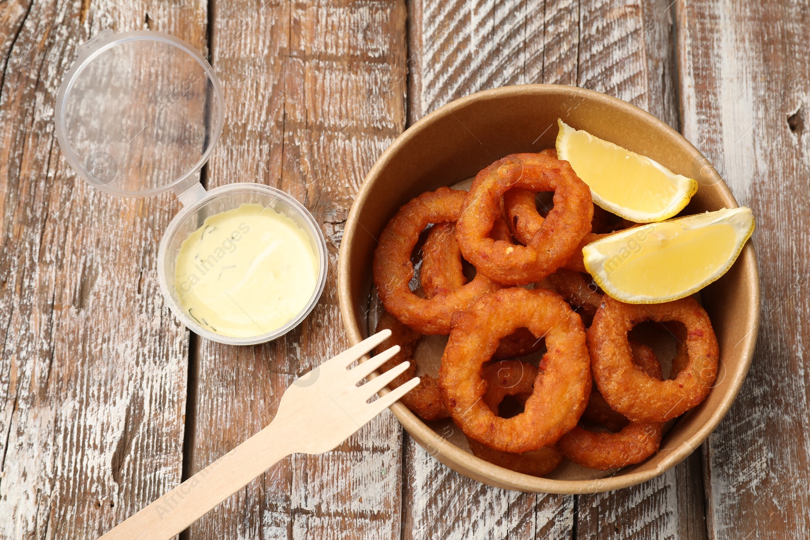 Photo of Fried squid rings, lemon and sauce on wooden table, flat lay