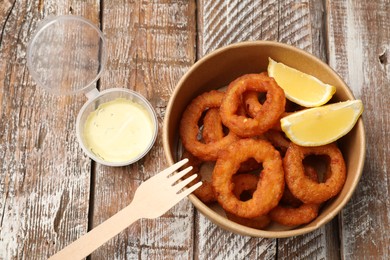 Photo of Fried squid rings, lemon and sauce on wooden table, flat lay