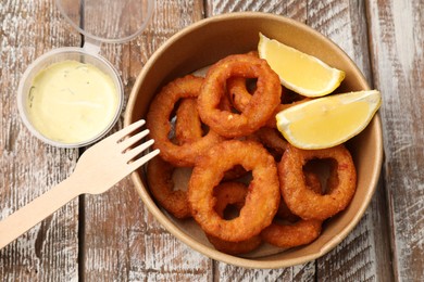 Photo of Fried squid rings, lemon and sauce on wooden table, flat lay