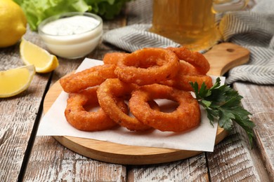 Photo of Fried squid rings served with sauce on wooden table, closeup