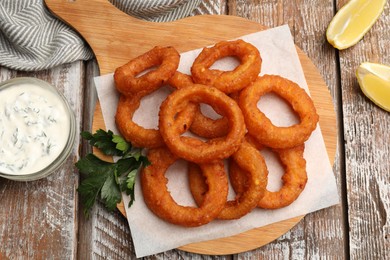 Photo of Fried squid rings served with sauce on wooden table, flat lay