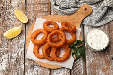 Photo of Fried squid rings served with sauce on wooden table, flat lay