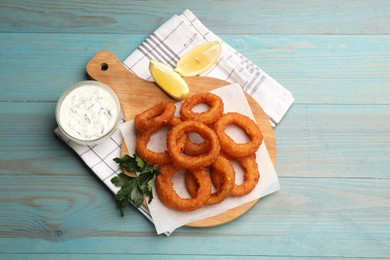 Photo of Fried squid rings served with sauce on light blue wooden table, flat lay