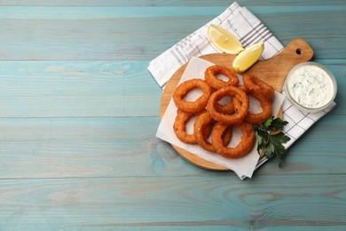 Photo of Fried squid rings served with sauce on light blue wooden table, flat lay. Space for text