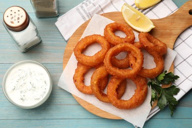 Photo of Fried squid rings served with sauce on light blue wooden table, flat lay