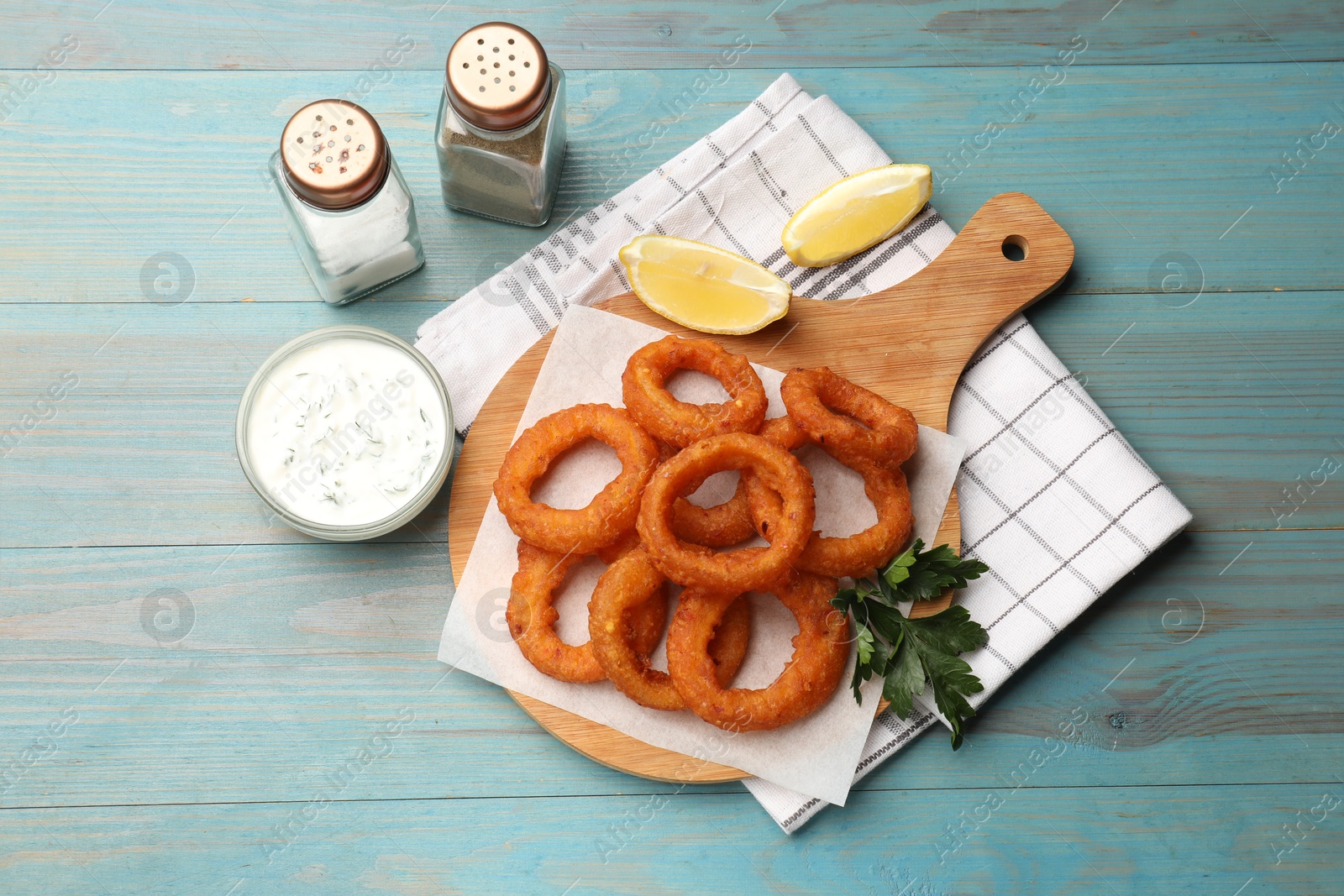 Fried squid rings served with sauce on light blue wooden table, flat lay Photo of Fried squid rings served with sauce on light blue wooden table, flat lay
