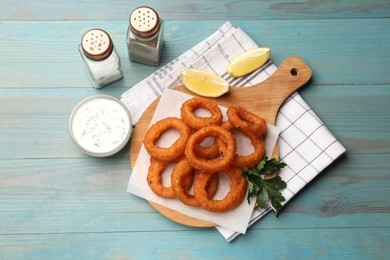Photo of Fried squid rings served with sauce on light blue wooden table, flat lay