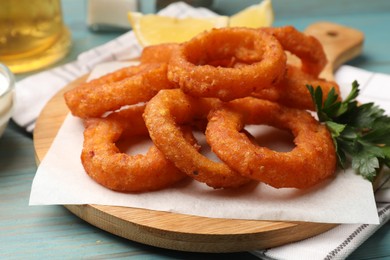Photo of Fried squid rings, parsley and lemon on light blue wooden table, closeup