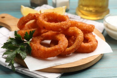 Photo of Fried squid rings served on light blue wooden table, closeup