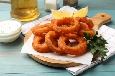 Photo of Fried squid rings served on light blue wooden table, closeup
