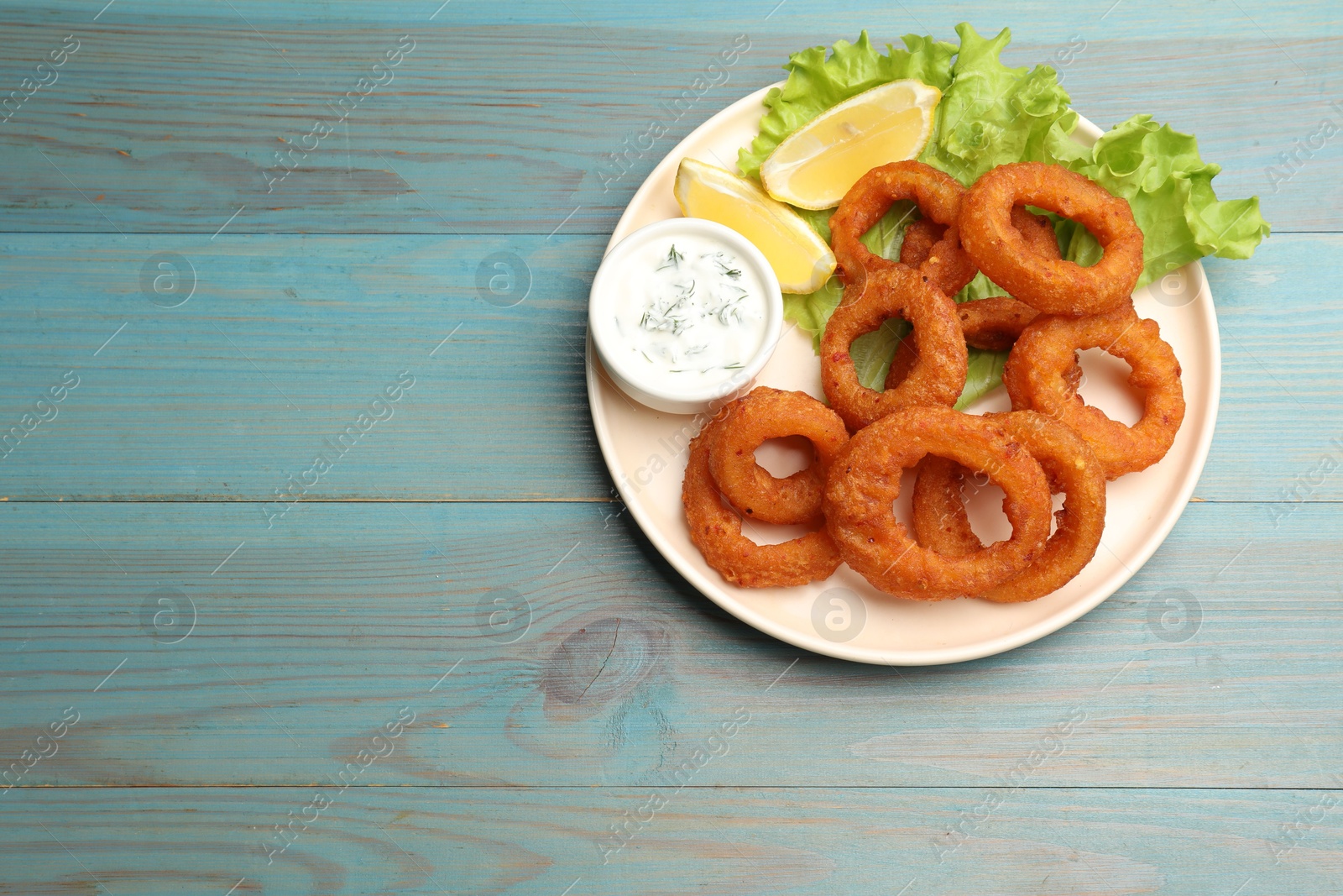 Fried squid rings served with sauce on light blue wooden table, top view. Space for text Photo of Fried squid rings served with sauce on light blue wooden table, top view. Space for text