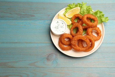 Photo of Fried squid rings served with sauce on light blue wooden table, top view. Space for text
