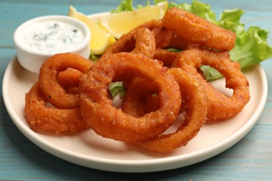Photo of Fried squid rings served with sauce on light blue wooden table, closeup