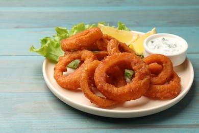 Photo of Fried squid rings served with sauce on light blue wooden table, closeup