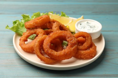 Photo of Fried squid rings served with sauce on light blue wooden table, closeup