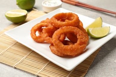 Photo of Fried squid rings, lime, sauce and chopsticks on grey table, closeup