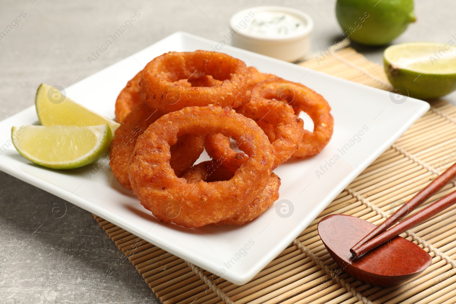 Photo of Fried squid rings, lime, sauce and chopsticks on grey table, closeup