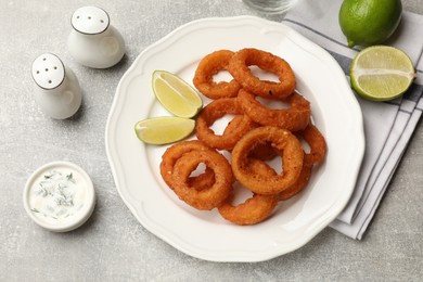Photo of Fried squid rings, lime and sauce on grey table, flat lay