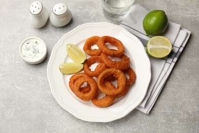 Photo of Fried squid rings, lime and sauce on grey table, flat lay