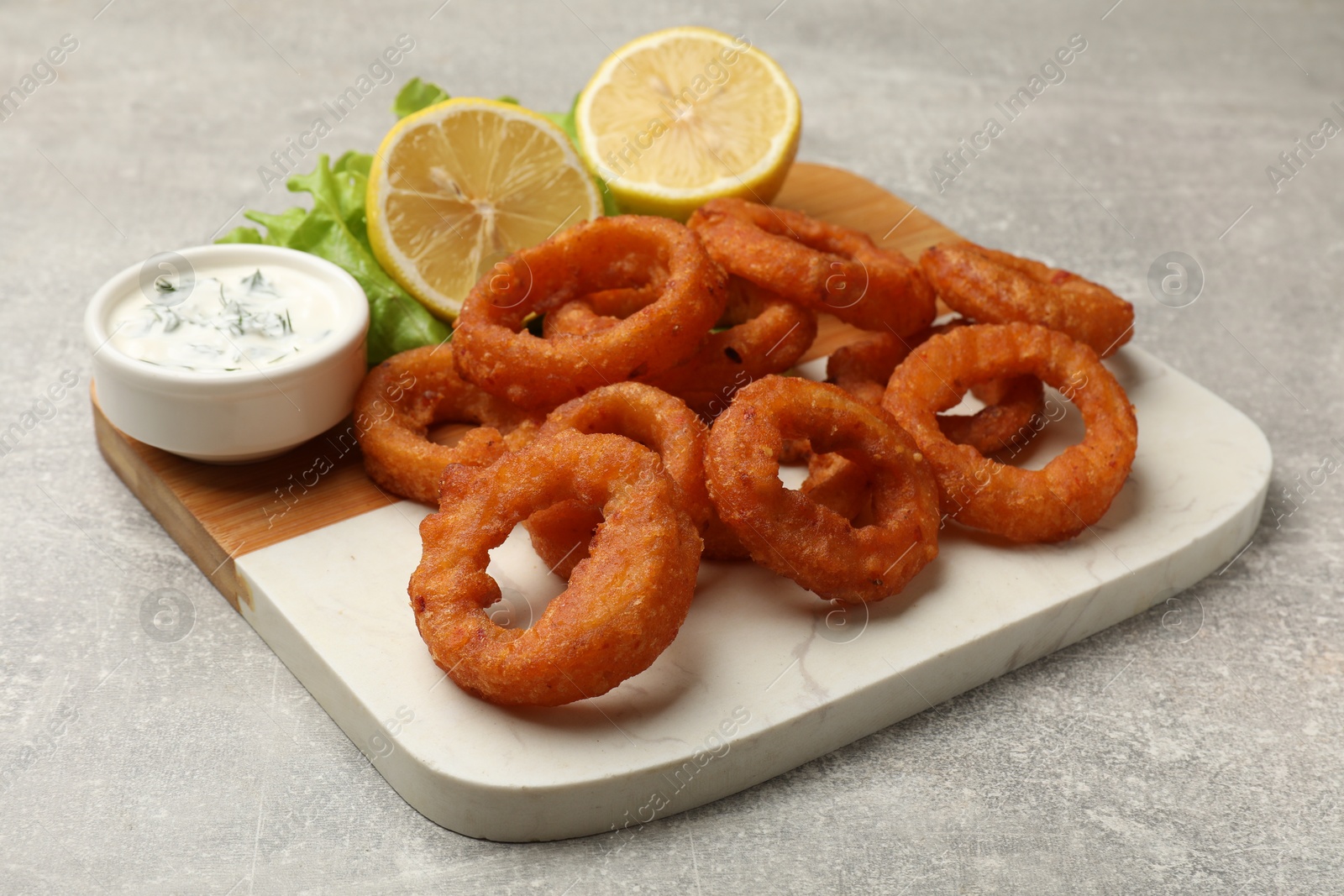 Photo of Fried squid rings, lemon, lettuce and sauce on grey table, closeup