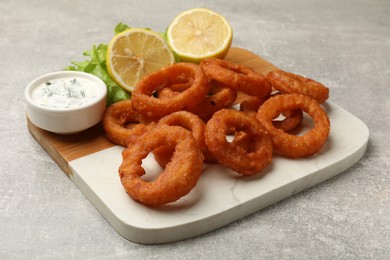 Photo of Fried squid rings, lemon, lettuce and sauce on grey table, closeup