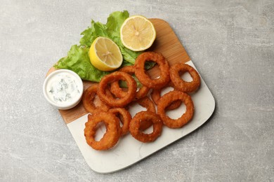 Photo of Fried squid rings, lemon, lettuce and sauce on grey table, top view