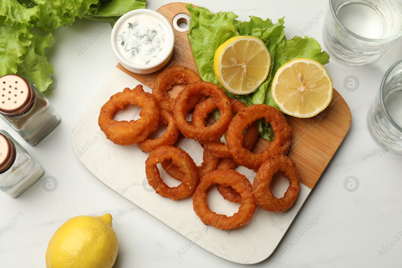 Photo of Fried squid rings served with sauce on white marble table, flat lay