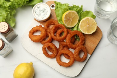 Photo of Fried squid rings served with sauce on white marble table, flat lay