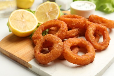 Photo of Fried squid rings served with sauce on white table, closeup