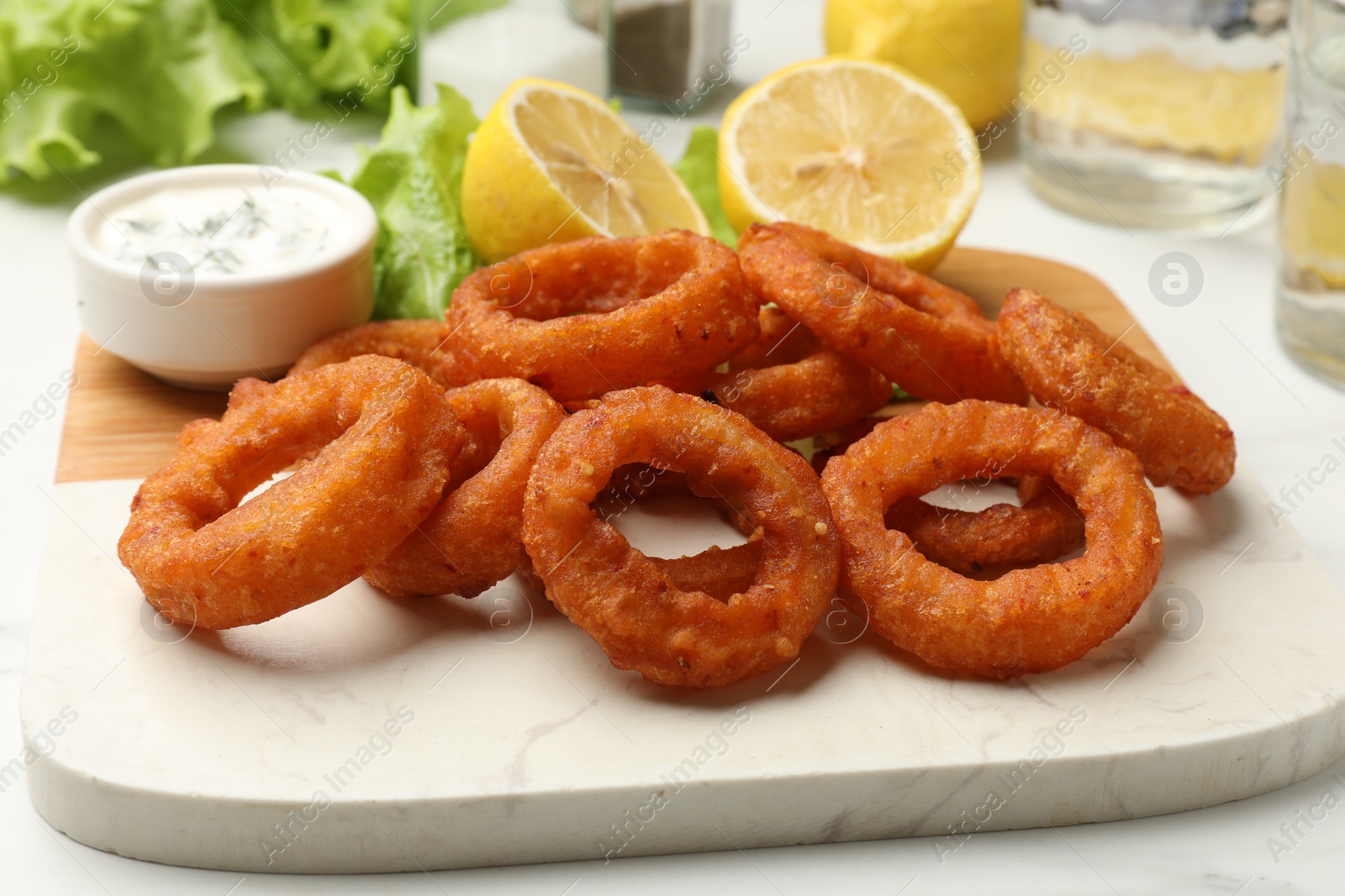 Photo of Fried squid rings served with sauce on white table, closeup