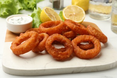 Photo of Fried squid rings served with sauce on white table, closeup