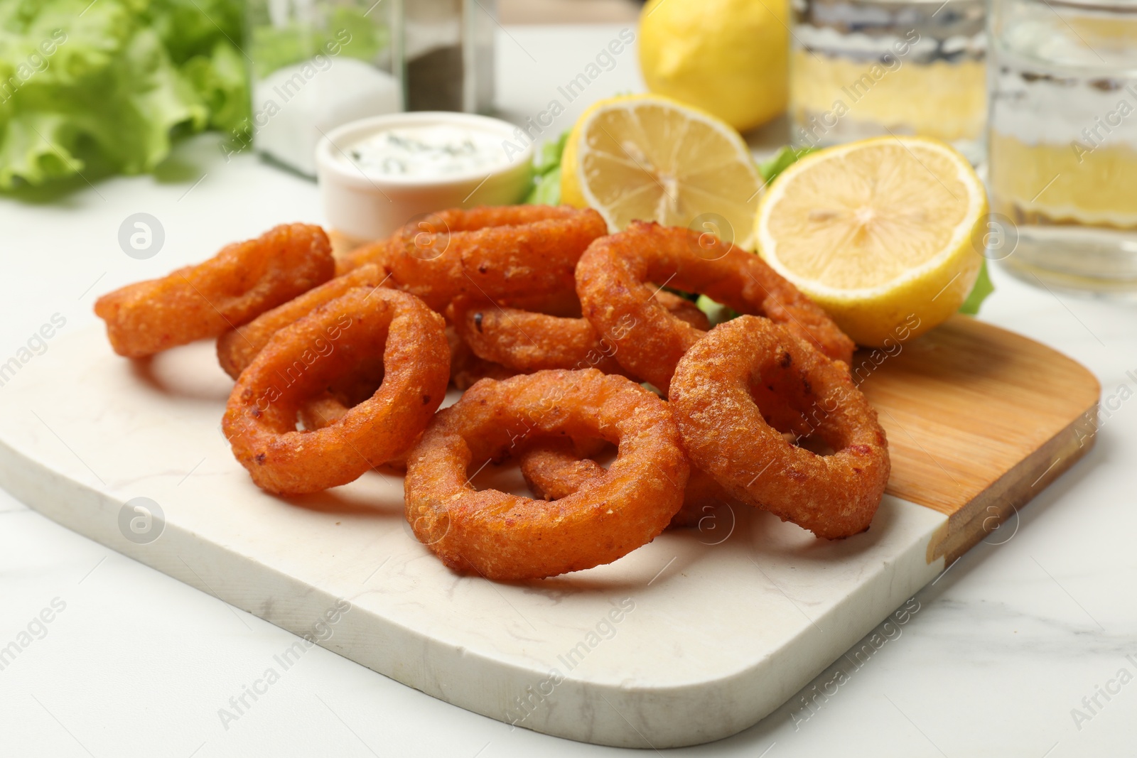 Photo of Fried squid rings served with sauce on white marble table, closeup